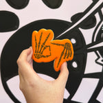 Hand holding an orange skeleton hand-shaped cookie against a black and white abstract background