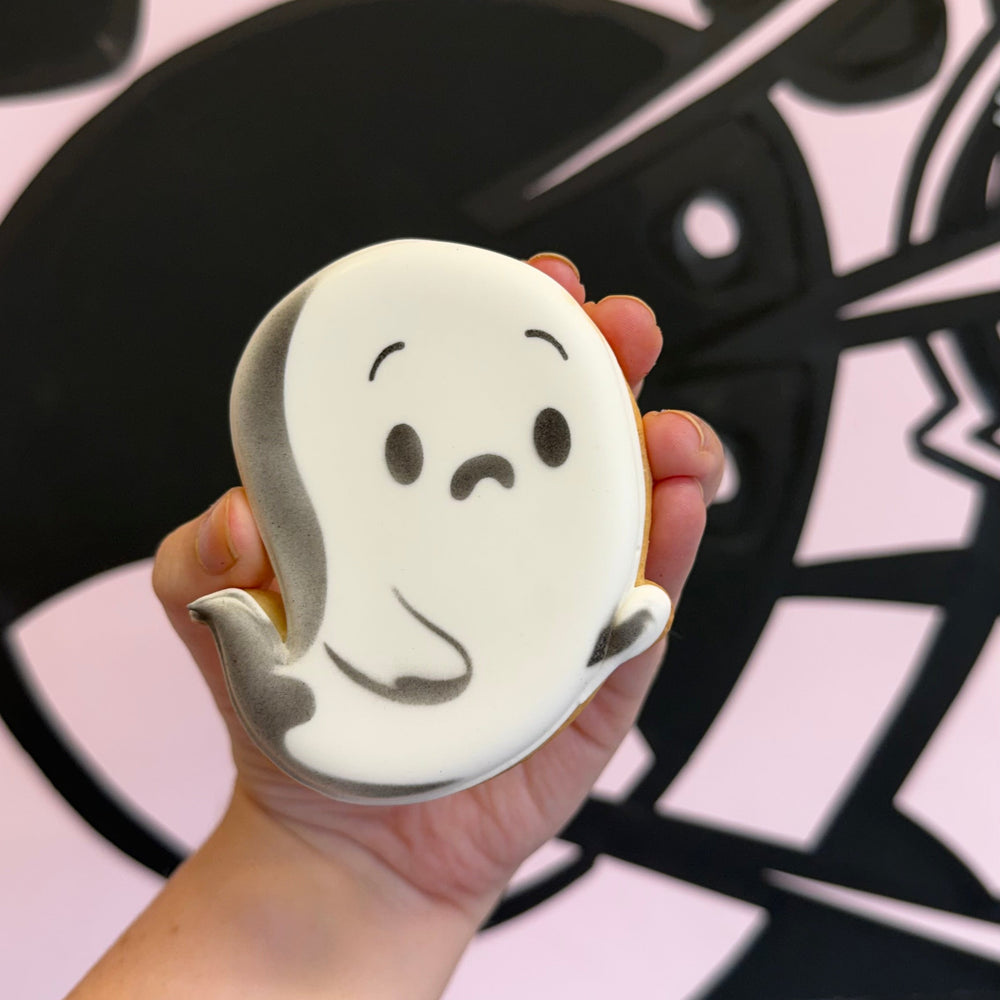 Hand holding a cookie with a ghost face design against a black and white abstract background.